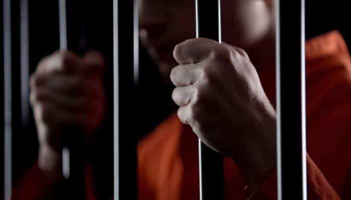 Person behind jail bars, representing the risk of incarceration associated with misdemeanor charges.