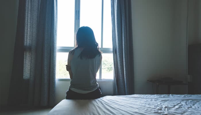 Reclaiming Touch On Your Terms - Mylegalopinion 1 - My Legal Opinion Woman sitting alone on a bed, gazing out the window, reflecting on the emotional impact of sexual trauma.