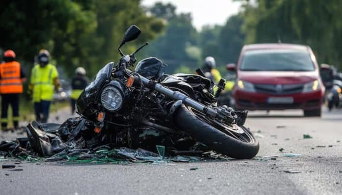 Motorcycle accident scene showing a damaged motorcycle on the road with emergency responders and vehicles in the background