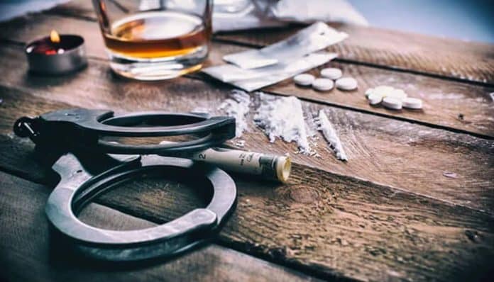 Drugs, handcuffs, and cash on a table representing evidence used in Possession vs Distribution Under California Law cases.