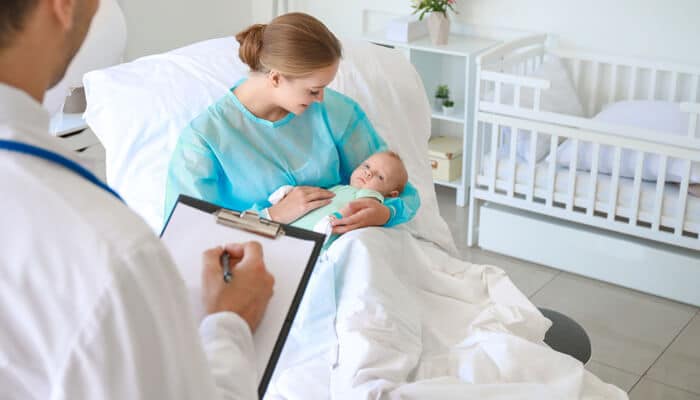 When Medical Records Dont Match Memories - Myleagalopinion - My Legal Opinion Mother holding newborn while a doctor reviews medical notes in a hospital room, a scenario often examined during a Birth Injury Claim.