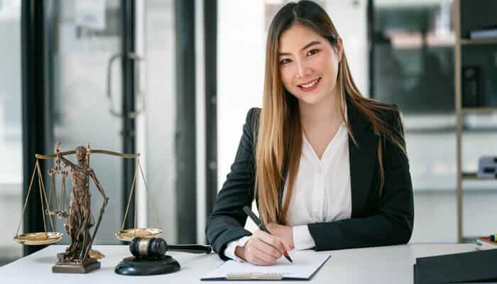 A female lawyer sitting at her desk with a scale of justice and gavel, smiling while preparing to sign legal documents. A great example of professionalism when hiring a lawyer.