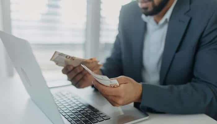 Professional at Legacy Professionals LLP handling cash and working on a laptop to manage financial data.