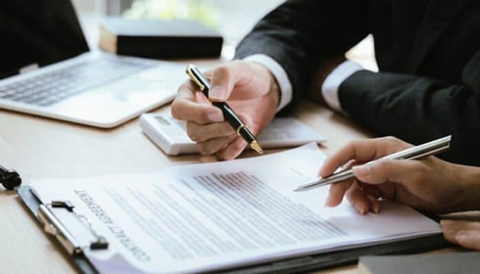 AZA Law legal professionals reviewing and signing a contract document in a corporate office setting with laptop and paperwork.