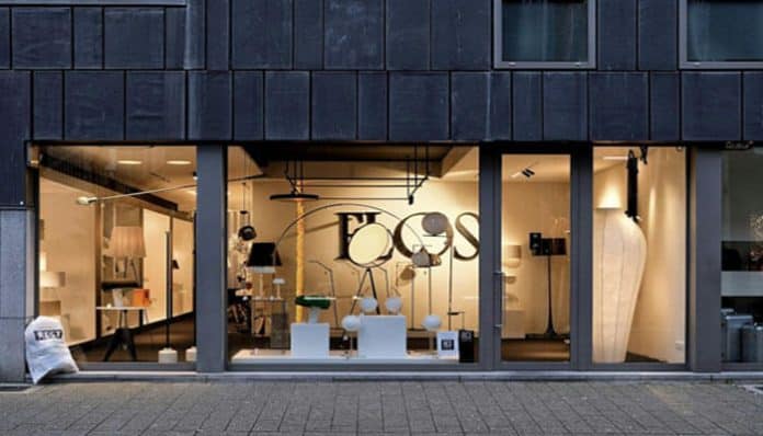 Storefront lighting showroom with glass façade; inside are lamps and fixtures arranged on white pedestals, a large BOSS logo on the back wall.