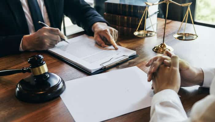 How New York Determines a Fair Division - Tycoonstory - My Legal Opinion Attorney signs documents across from a client at a wooden desk, with a gavel, scales, and stack of books visible nearby.