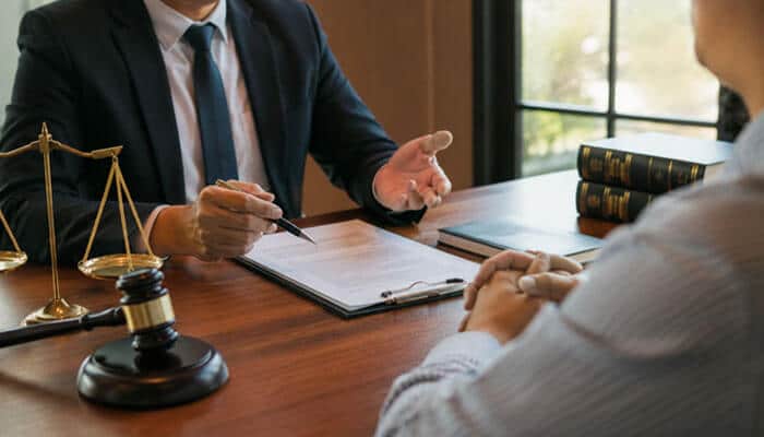 The Case for Professional Representation - My Legal Opinion - My Legal Opinion Lawyer in a suit discusses documents with a client across a wooden desk, with scales of justice and a gavel nearby.